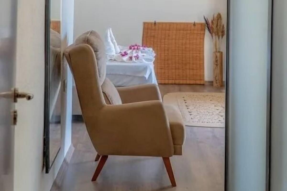 Una habitación moderna con un espejo grande, dos sillones color beige, una mesita con mantel blanco y dos lámparas colgantes de mimbre.