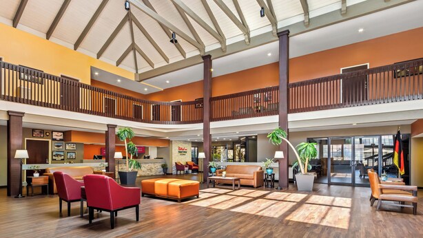 A spacious lobby with a high ceiling, wooden flooring, and multiple seating areas including red chairs and a sofa. - Red Roof Inn Ridgecrest (Ridgecrest)
