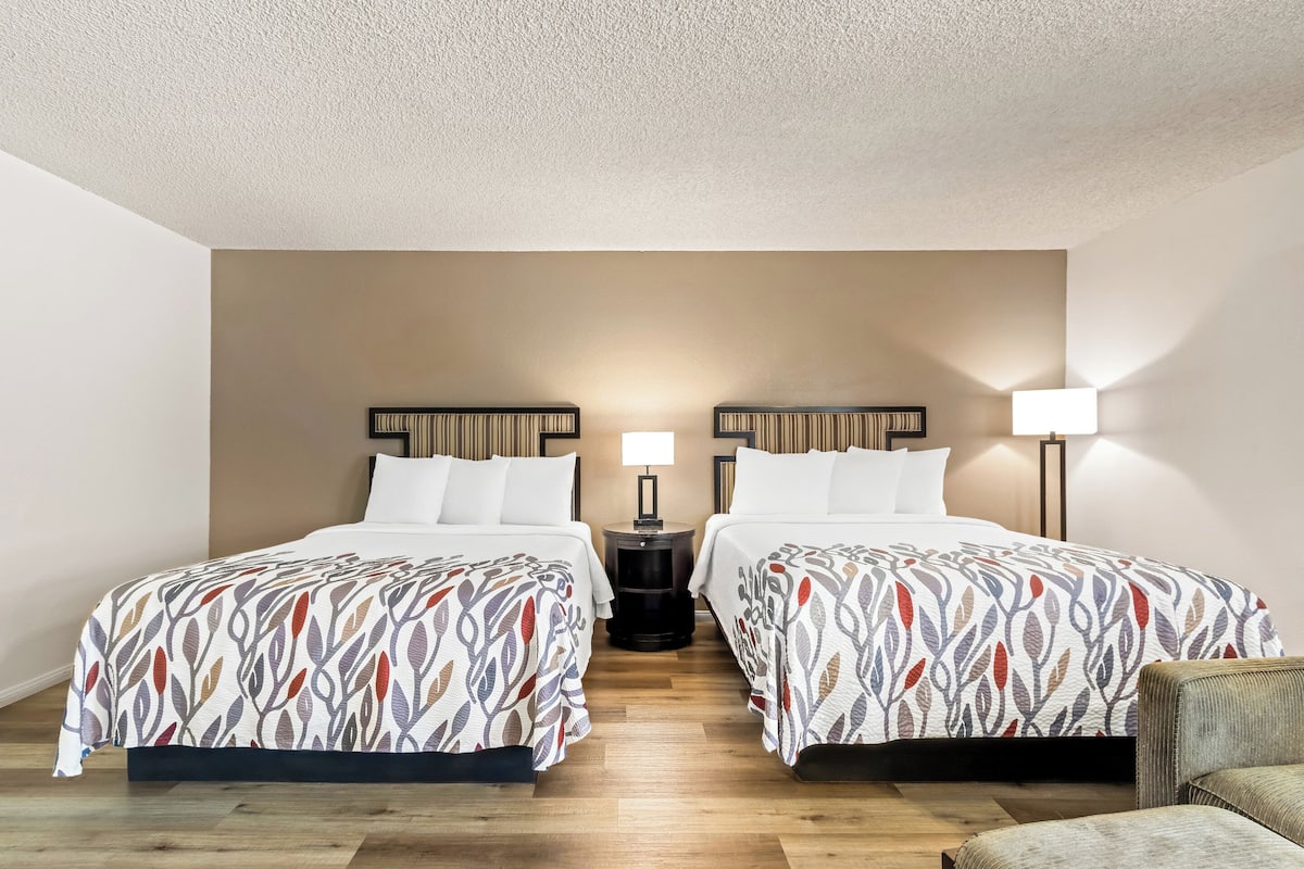 Una habitación de hotel con dos camas, una mesita de noche con lámpara y una silla.
