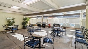 A covered patio area with tables and chairs, a grill, and potted plants. - Red Roof Inn Ridgecrest (Ridgecrest)