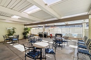 Un área de patio techada con mesas y sillas, una parrilla y plantas en macetas.