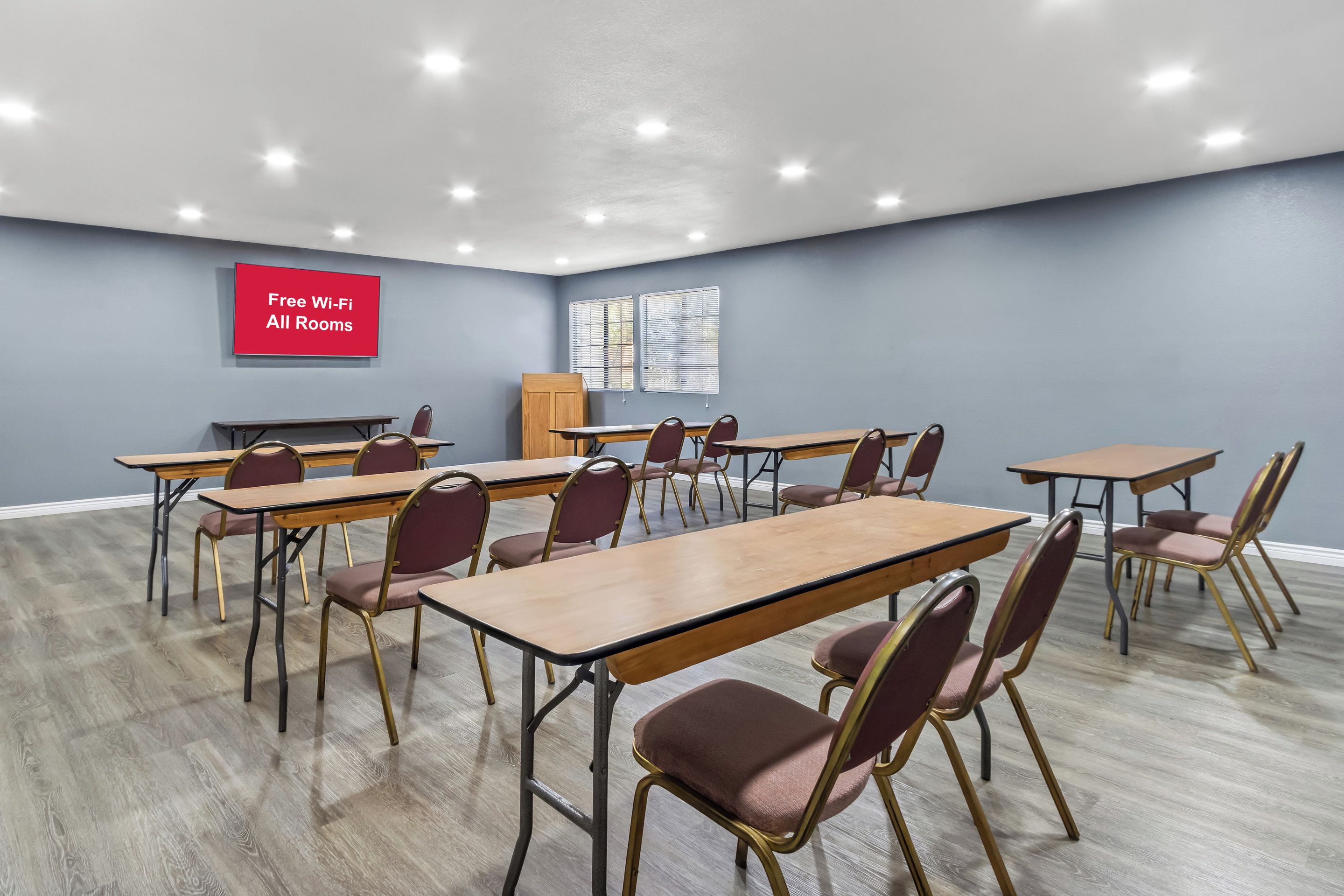 A conference room with tables and chairs, a red sign indicating free Wi-Fi, and a window with blinds.