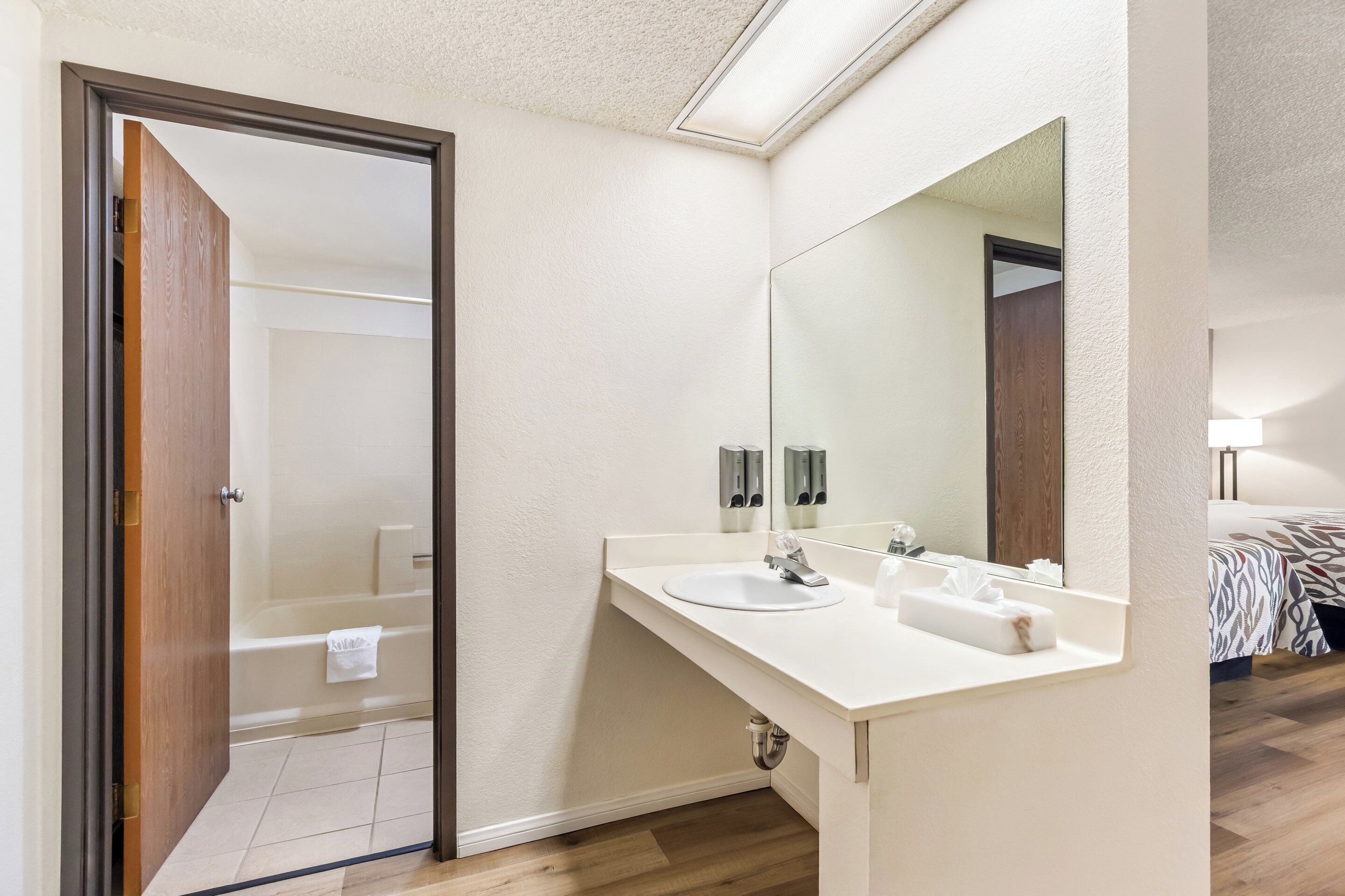 Un baño moderno con un lavabo blanco, un espejo grande y una ducha visible a través de una puerta abierta.