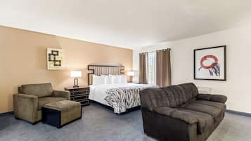 Une chambre d’hôtel comprenant un lit, deux fauteuils, un canapé, une petite table et une lampe.