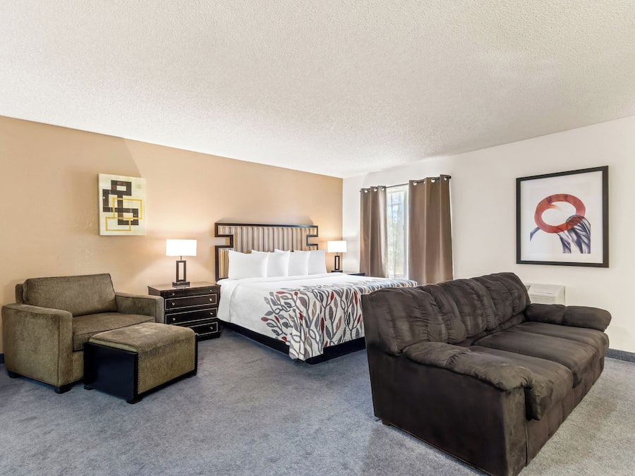 A hotel room with a bed, two armchairs, a sofa, a small table, and a lamp.