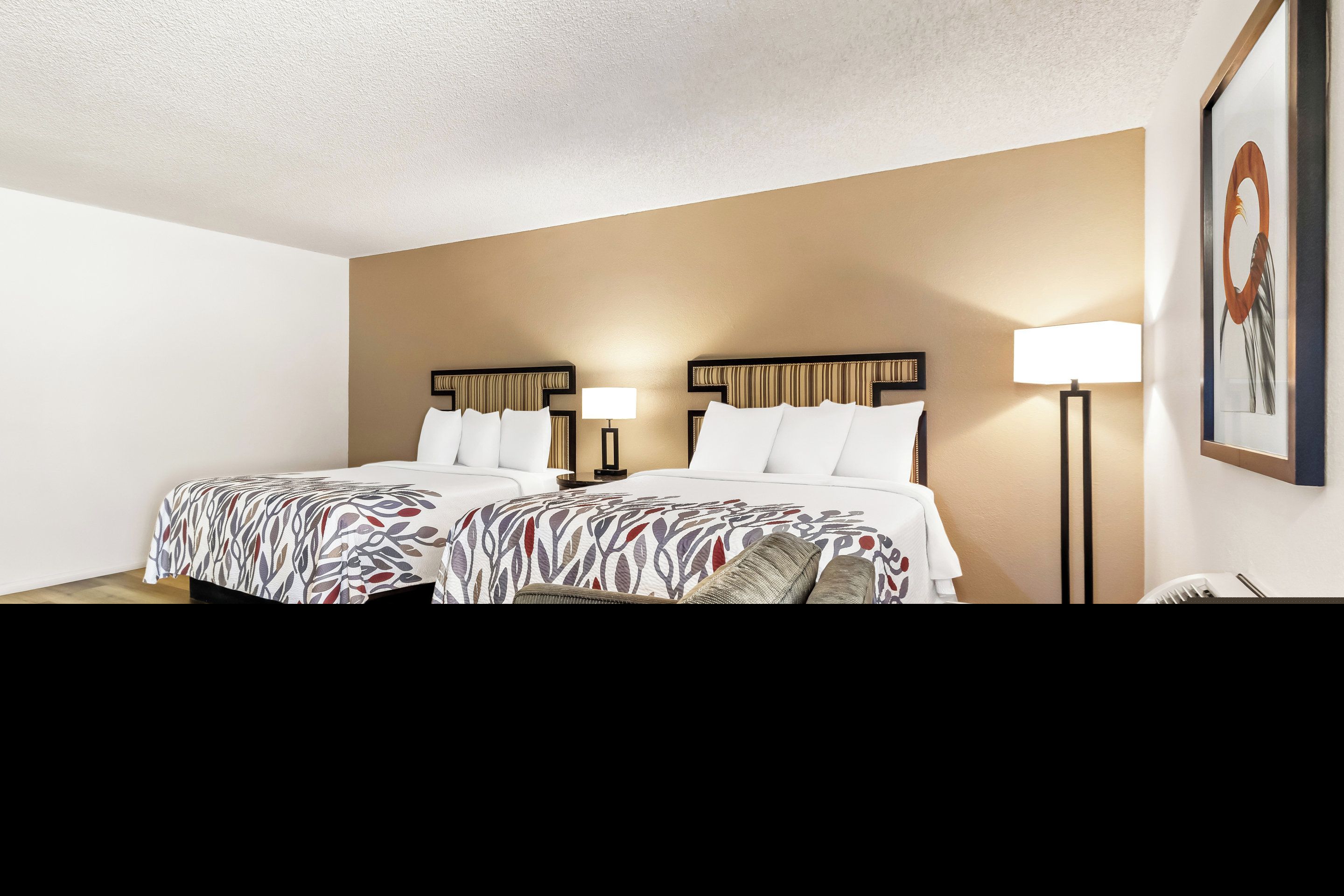A hotel room with two beds, a sofa, a standing lamp, and a wall-mounted air conditioner.