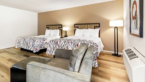 Ett hotellrum med två sängar, en soffa, en golvlampa och en väggmonterad luftkonditioneringsanläggning.