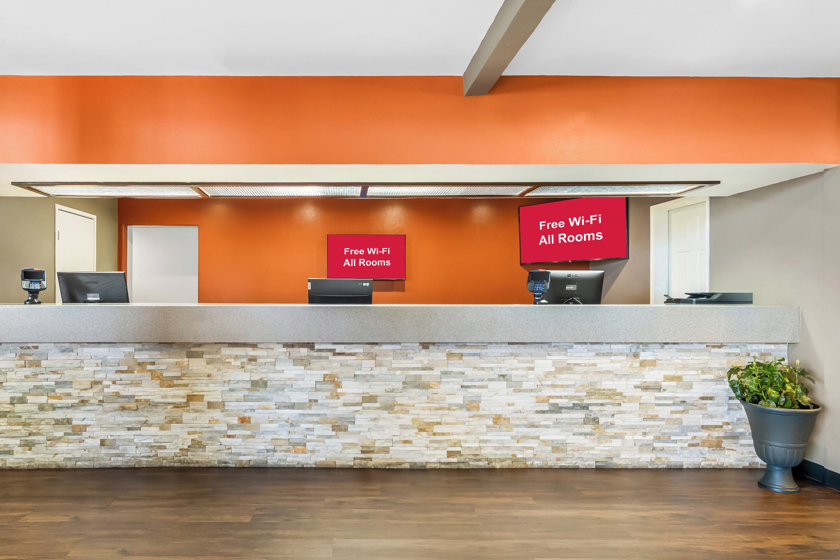 A reception area with a stone mosaic wall, two reception desks, and a sign indicating free Wi-Fi in all rooms.