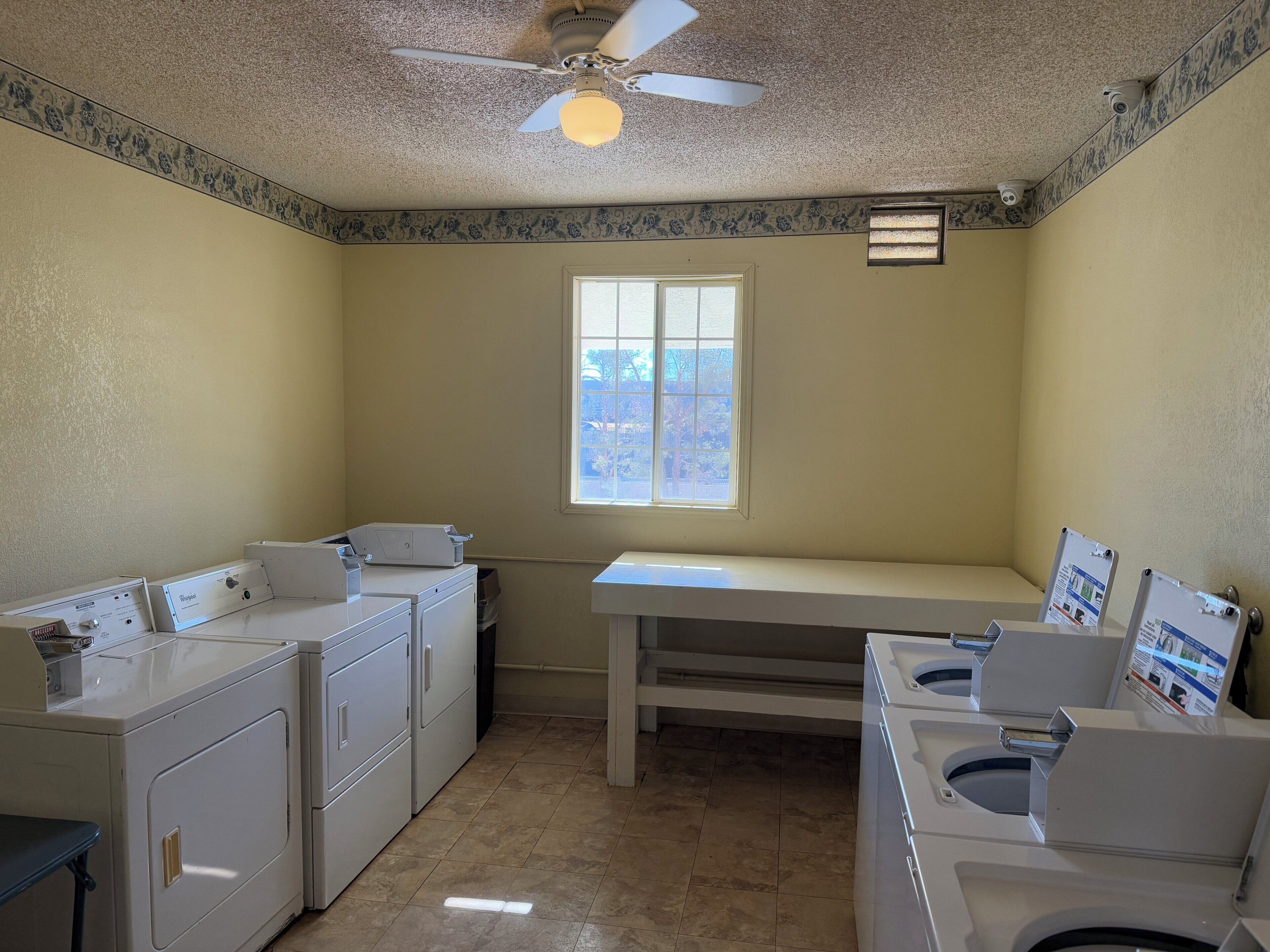 A laundry room with two washing machines, a ceiling fan, and a window.