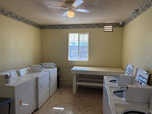 A laundry room with two washing machines, a ceiling fan, and a window.