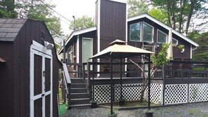 Ein modernes, zweistöckiges Haus mit überdachter Terrasse und einem kleinen Schuppen.