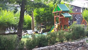 Ein Spielplatz mit Rutsche und Klettergerüsten, umgeben von Bäumen und einer Steinmauer.
