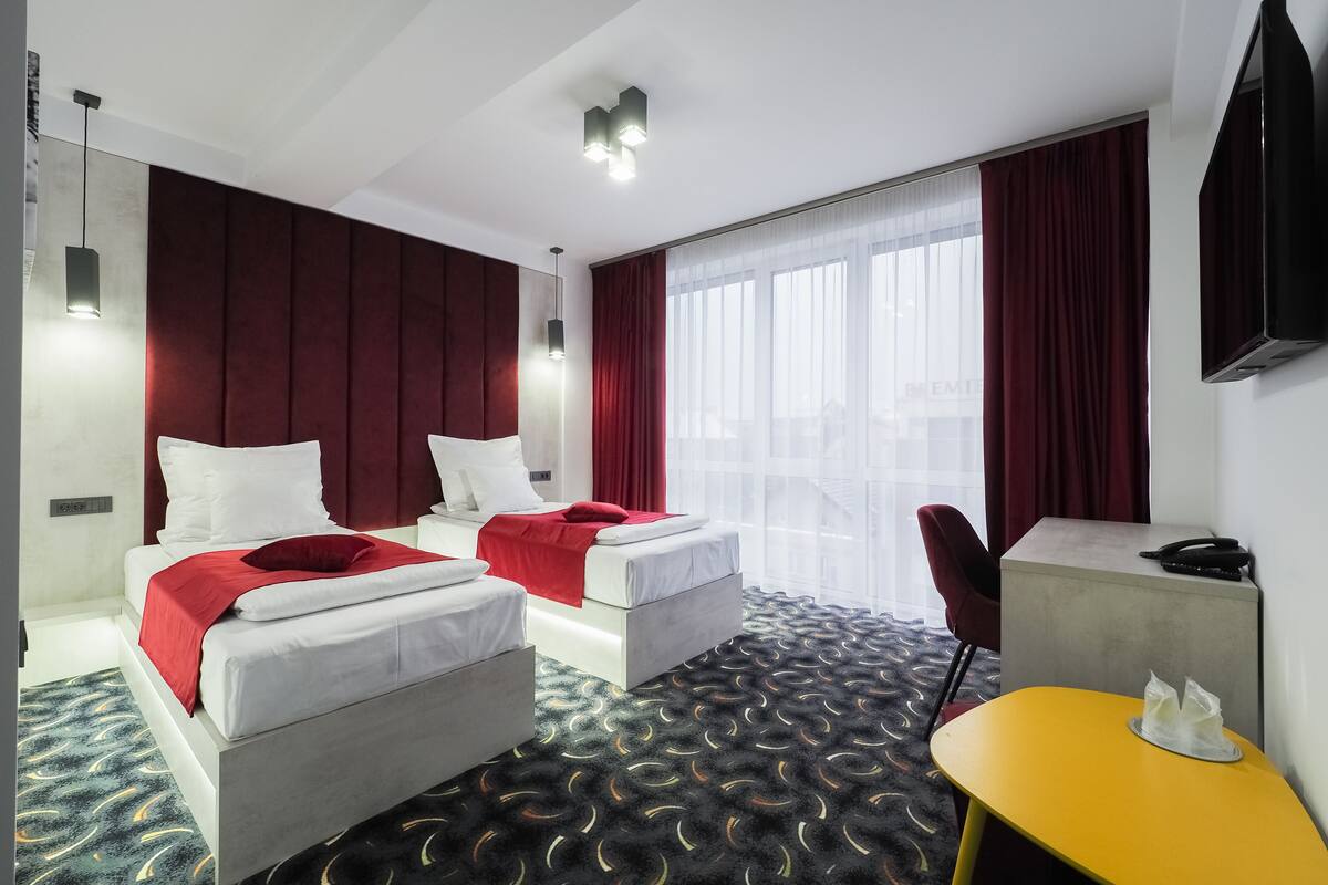 Une chambre d’hôtel avec deux lits, un bureau, une chaise, une télévision et une grande fenêtre avec des rideaux.