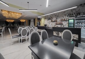 Zona de bar moderna con paredes de mármol, una araña y una variedad de botellas de licor.