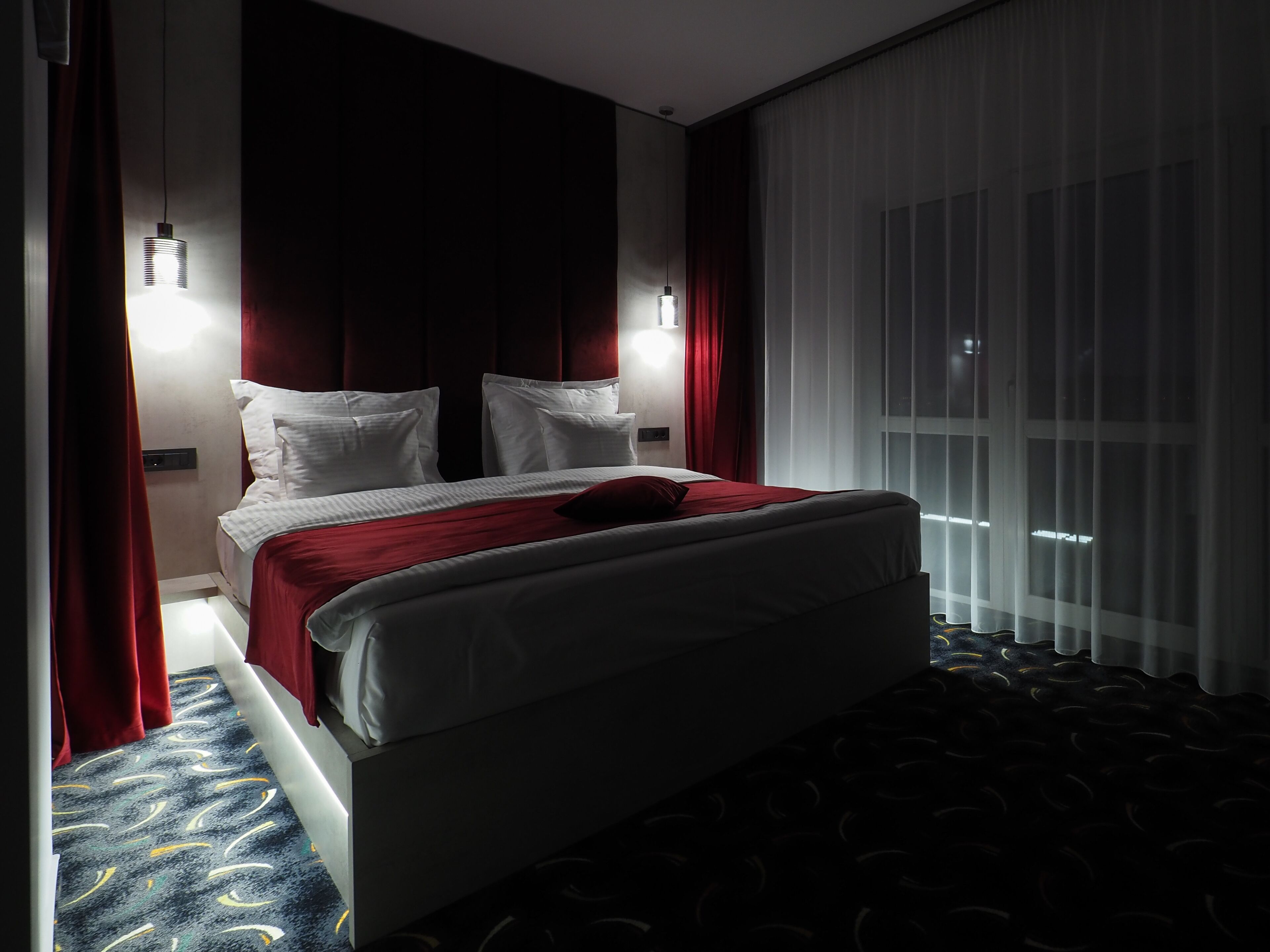 Una habitación de hotel moderna con una cama grande, cortinas rojas y vistas al cielo nocturno a través de la ventana.