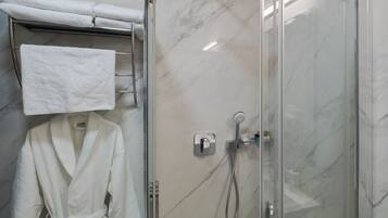 Una ducha con paredes de vidrio, un cabezal de ducha manual y un panel de control en la pared.