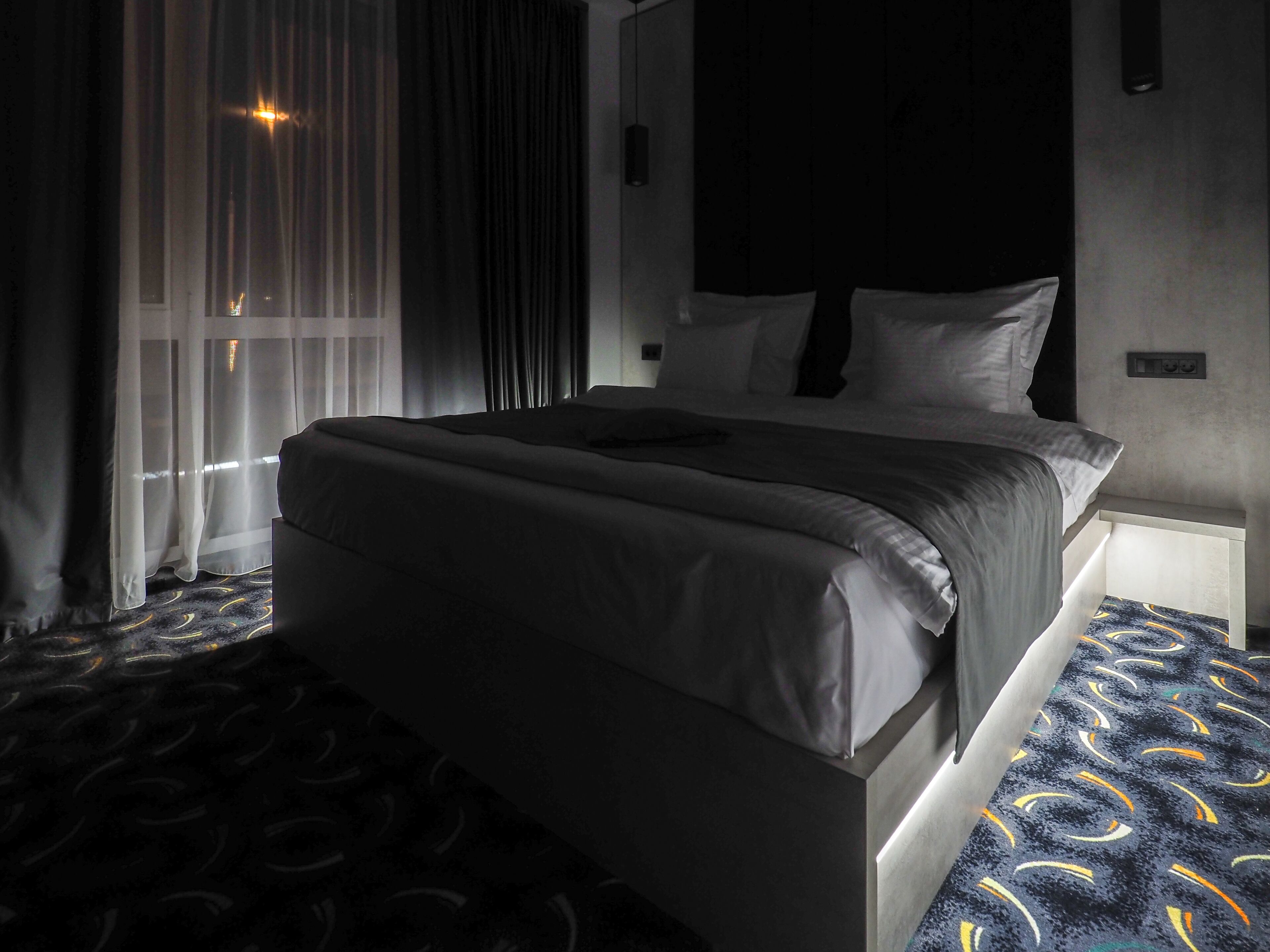 A hotel room with a large bed, a bedside table, and a window with curtains.