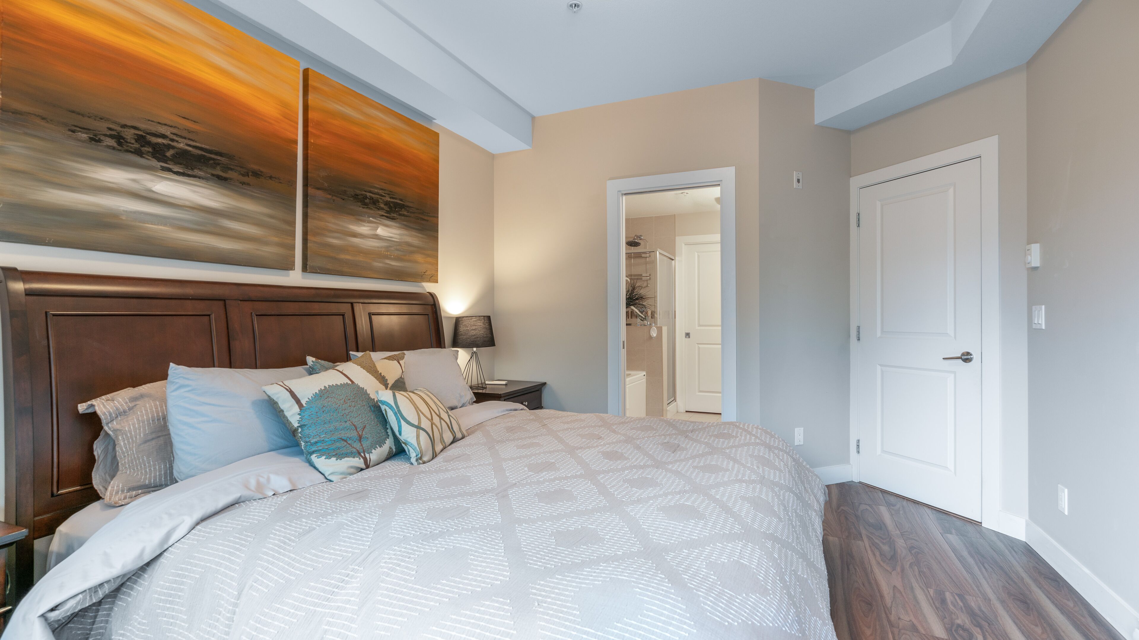 Un dormitorio con una cama grande, una mesita de noche, una lámpara de pared y una puerta que da al baño.