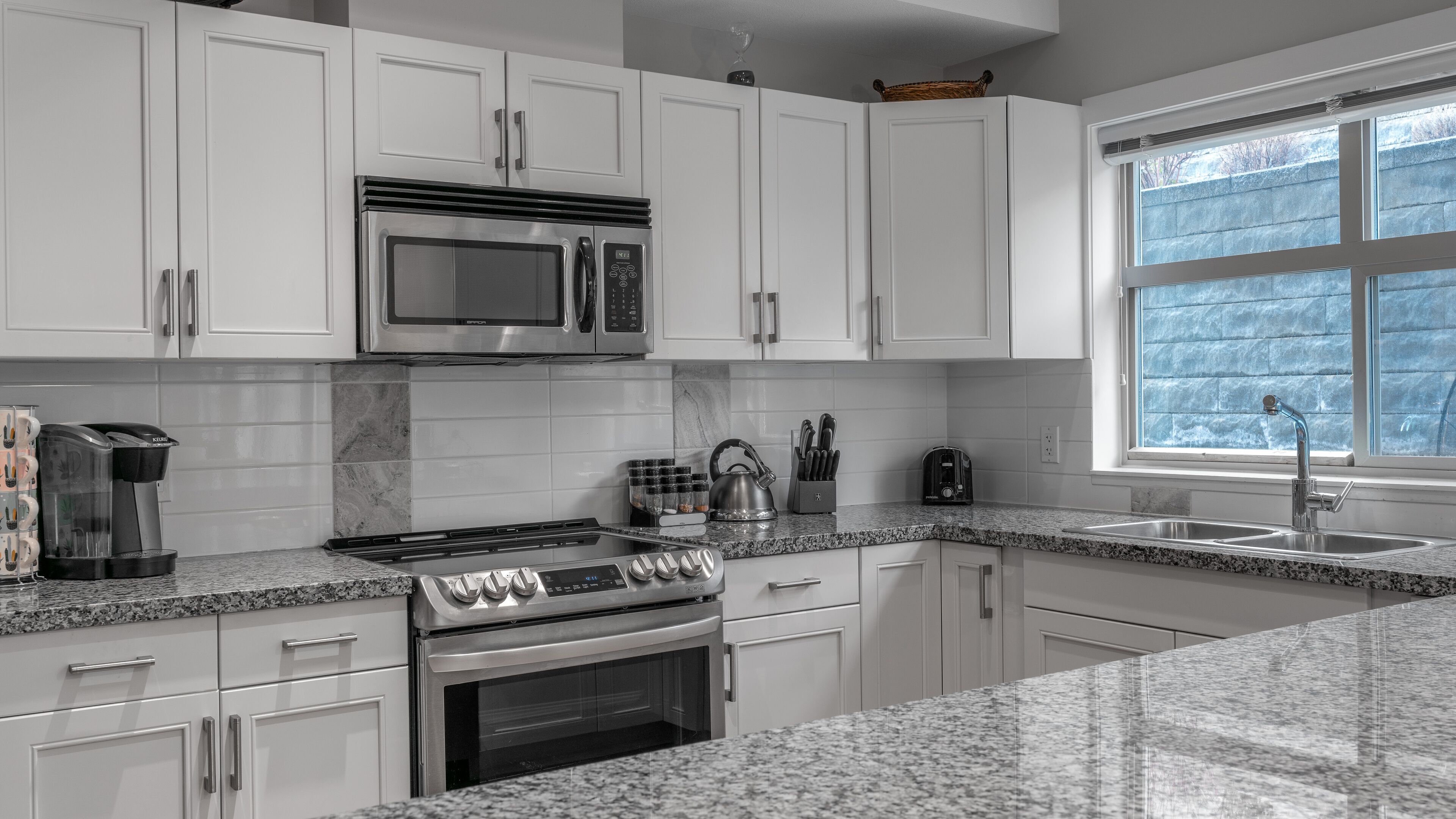 Una cocina moderna con armarios blancos, estufa de acero inoxidable, microondas y encimera de granito.