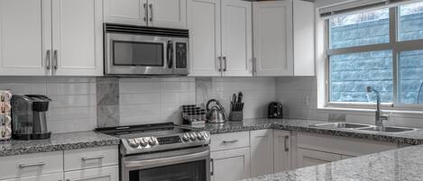 Una cocina moderna con armarios blancos, estufa de acero inoxidable, microondas y encimera de granito.
