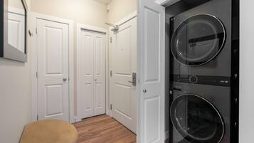 Una sala de lavandería con dos lavadoras de carga frontal apiladas, dos puertas blancas dobles y suelo de madera.