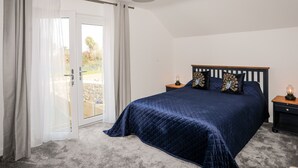 Un dormitorio con una cama grande, una mesita de noche, una lámpara y vistas a través de un ventanal.