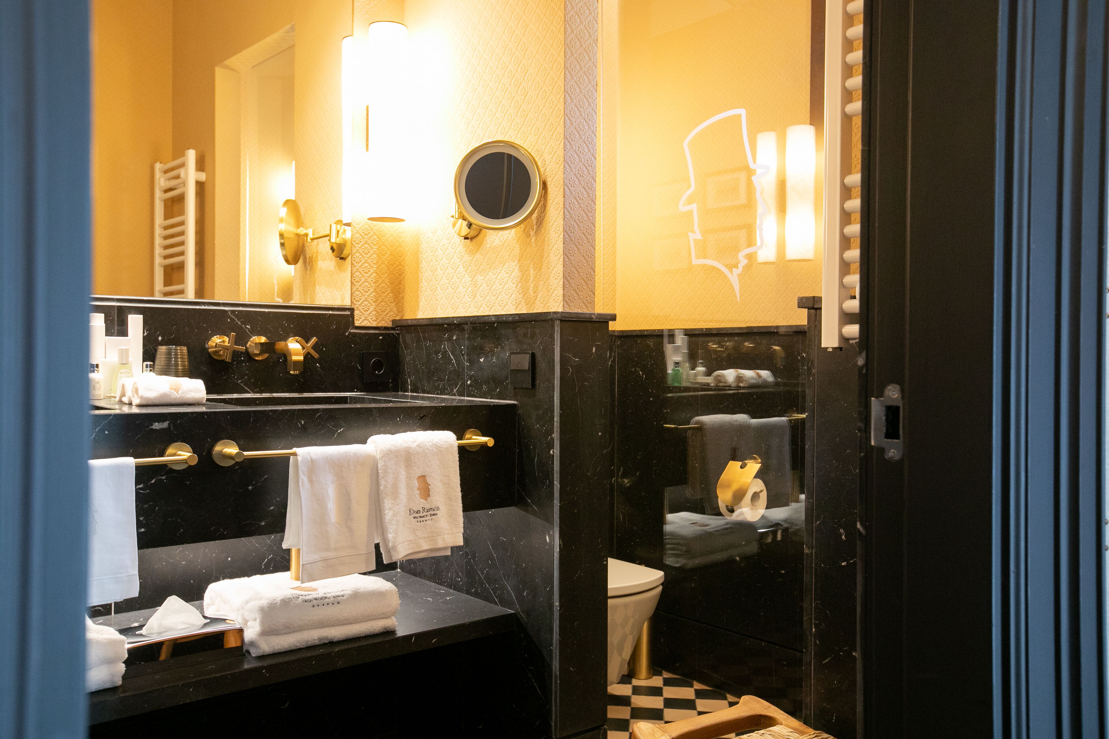 A bathroom with a black marble sink, gold fixtures, and a white towel rack.