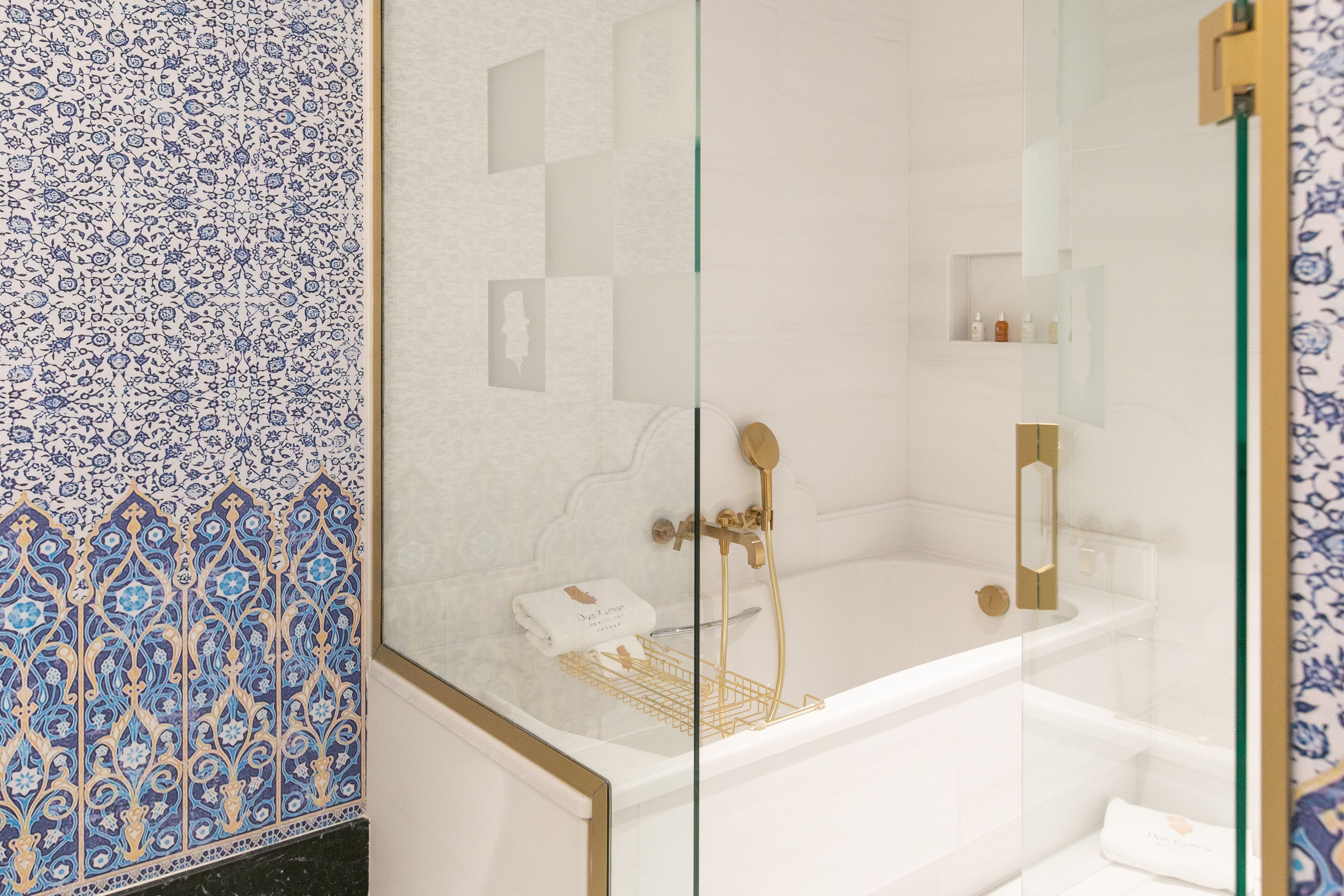 Un baño con una bañera blanca, una zona de ducha con mampara de vidrio y un revestimiento de pared con diseño.