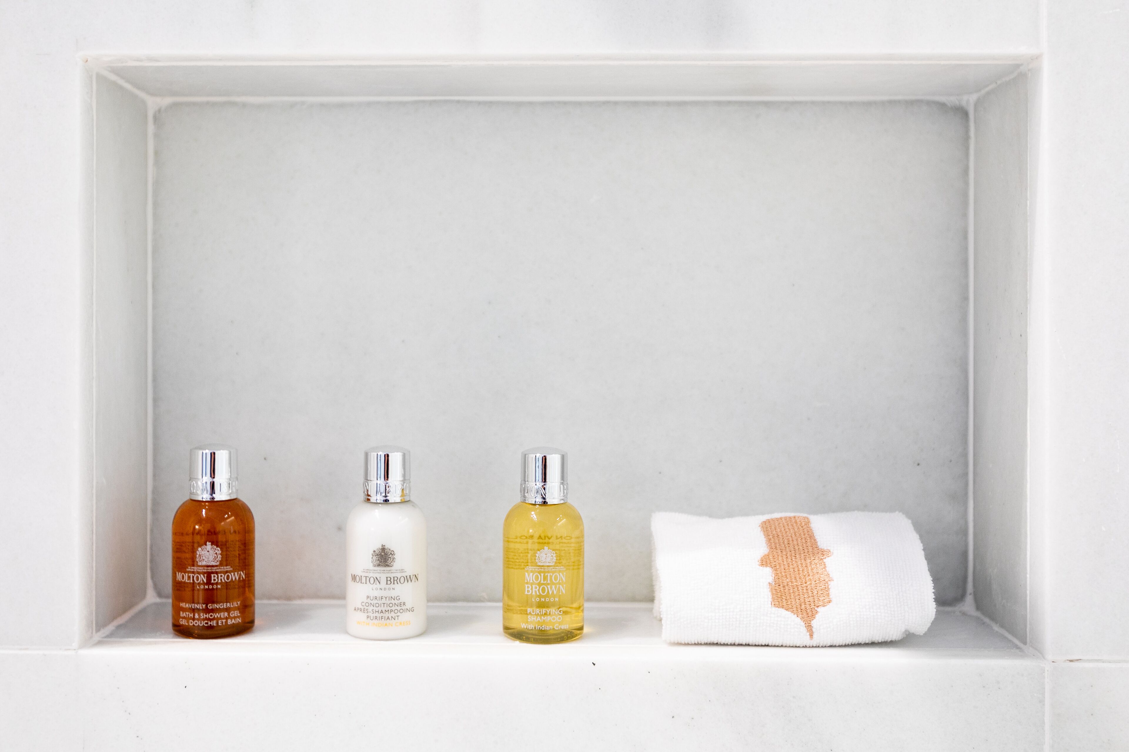 A bathroom shelf with three bottles of Molton Brown products and a white towel with an orange design.