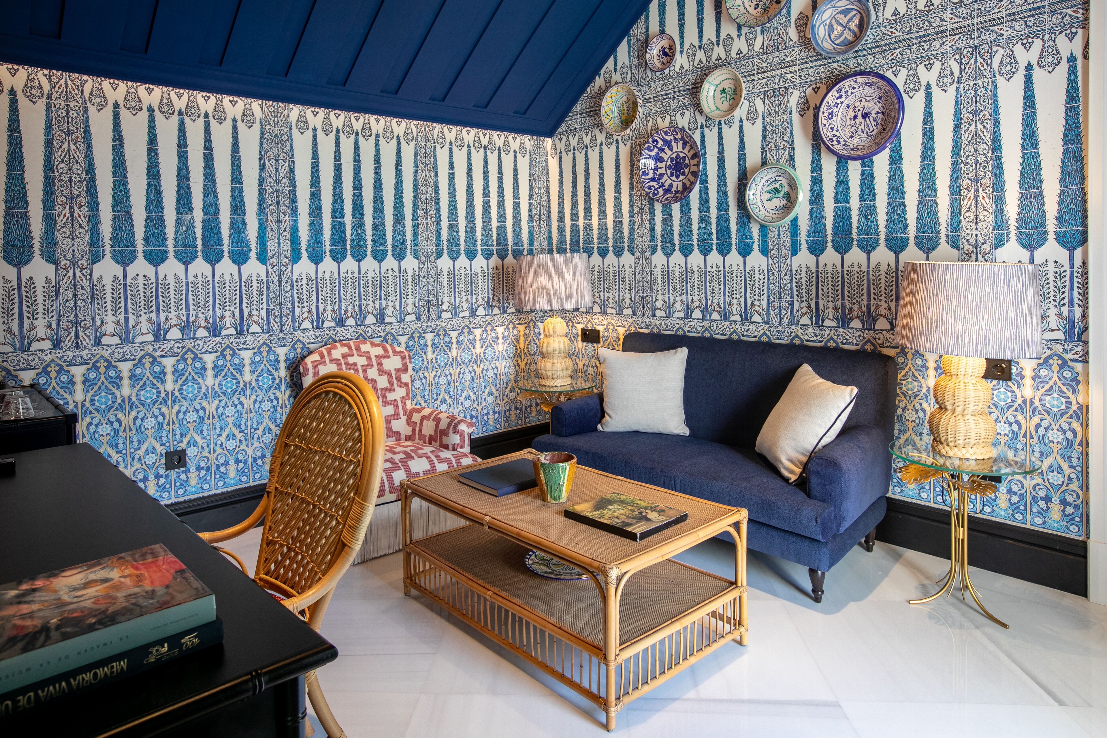 Una habitación con sofá azul, una mesita de centro de mimbre y papel tapiz estampado.