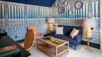 Una habitación con sofá azul, una mesita de centro de mimbre y papel tapiz estampado.