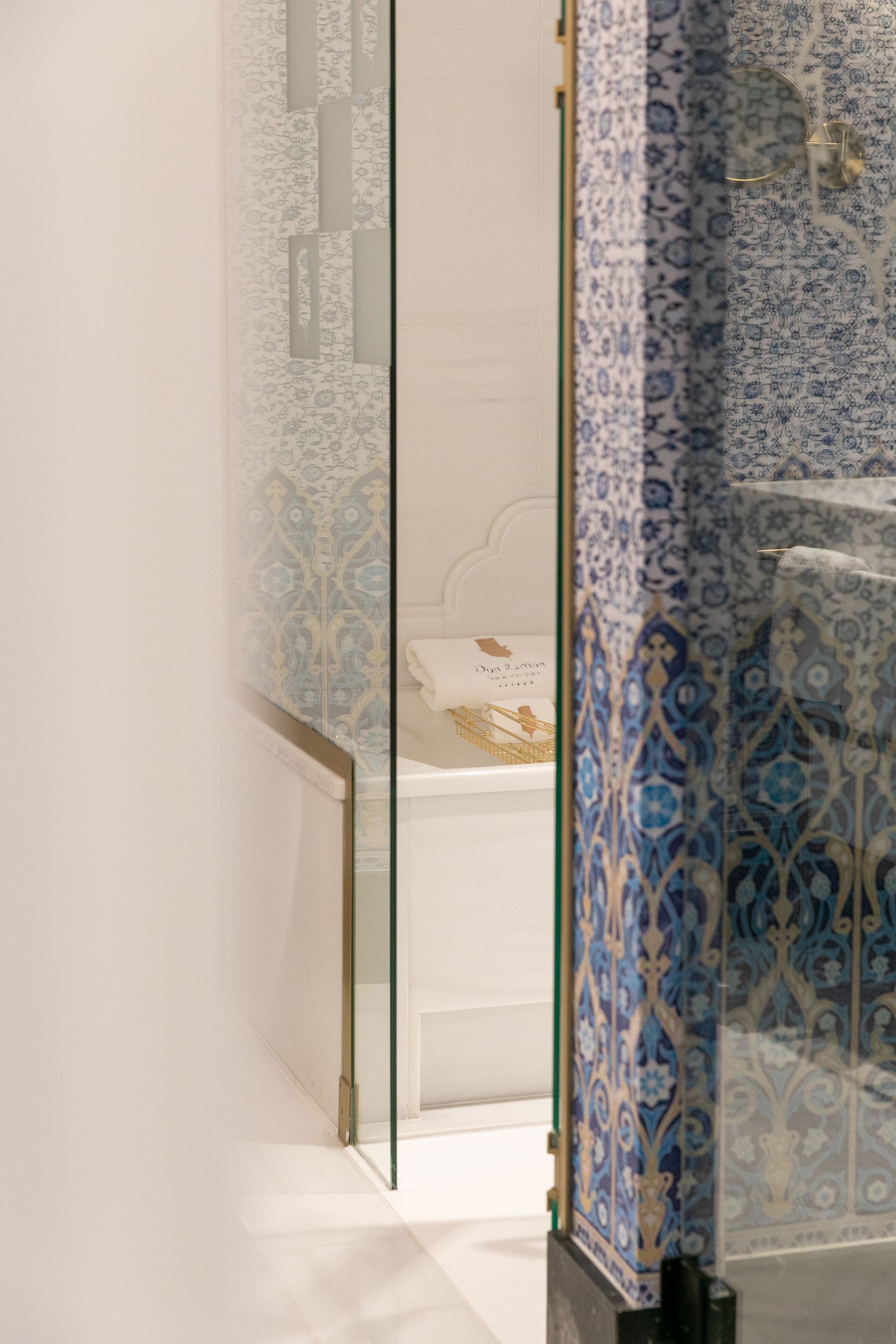 Un baño moderno con mampara de vidrio, una bañera y azulejos estampados.