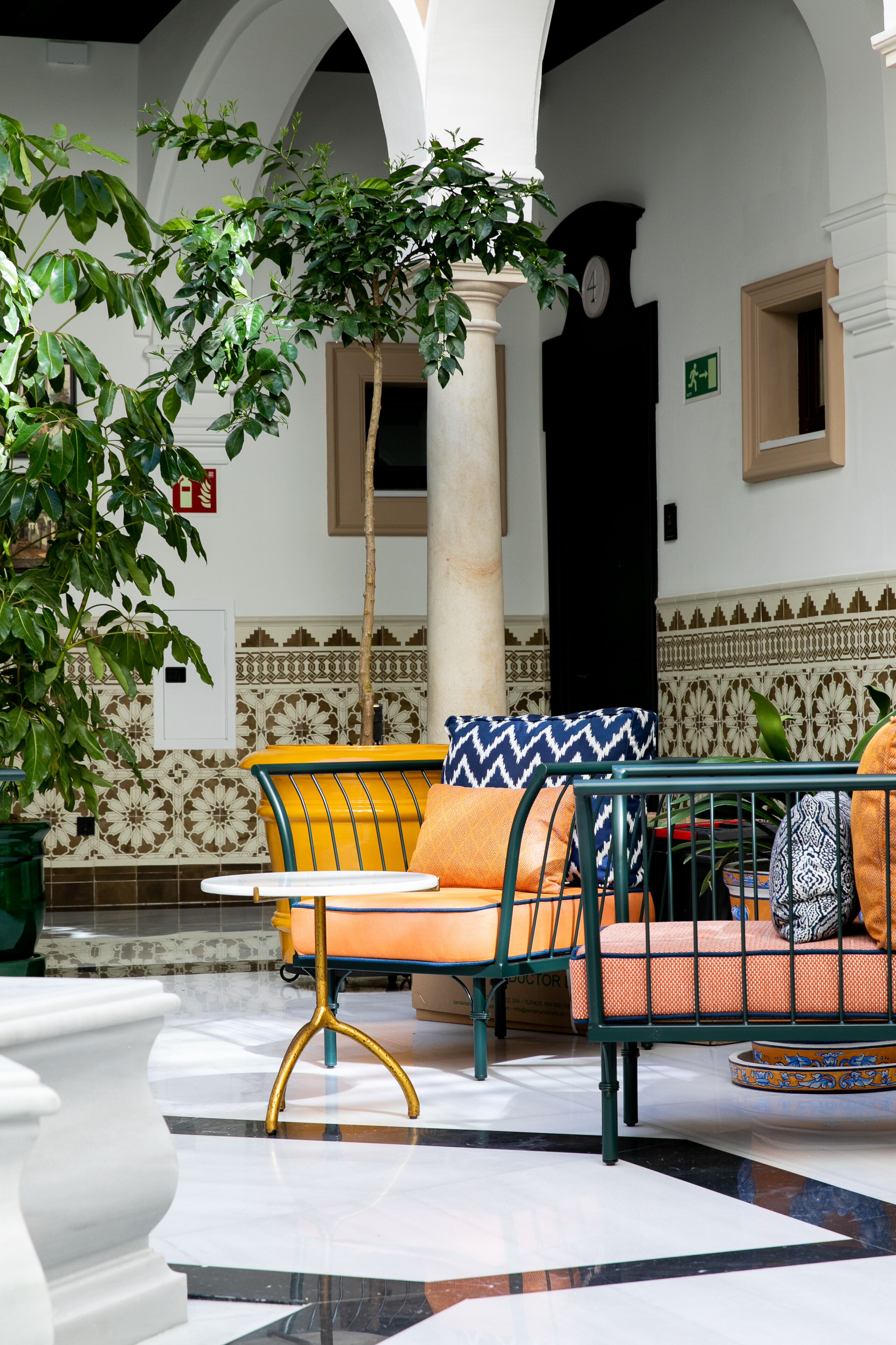 Un patio con zona de estar que incluye una silla con cojín de estampado amarillo y azul, una mesa y una planta en maceta.