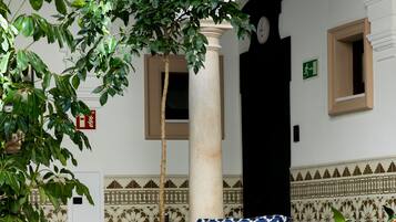 Un patio con zona de estar que incluye una silla con cojín de estampado amarillo y azul, una mesa y una planta en maceta.