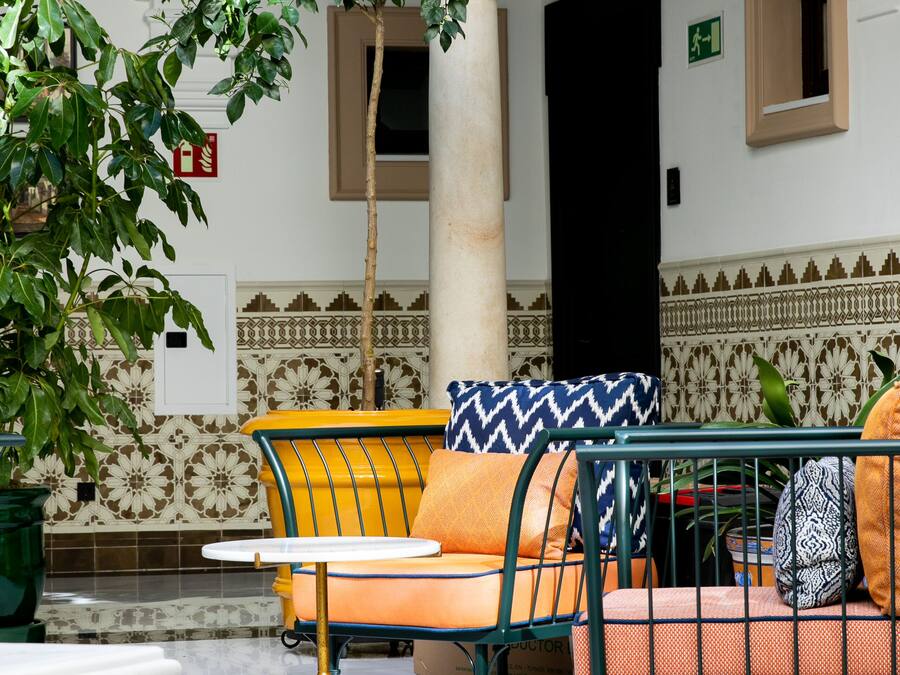 Un patio con zona de estar que incluye una silla con cojín de estampado amarillo y azul, una mesa y una planta en maceta.