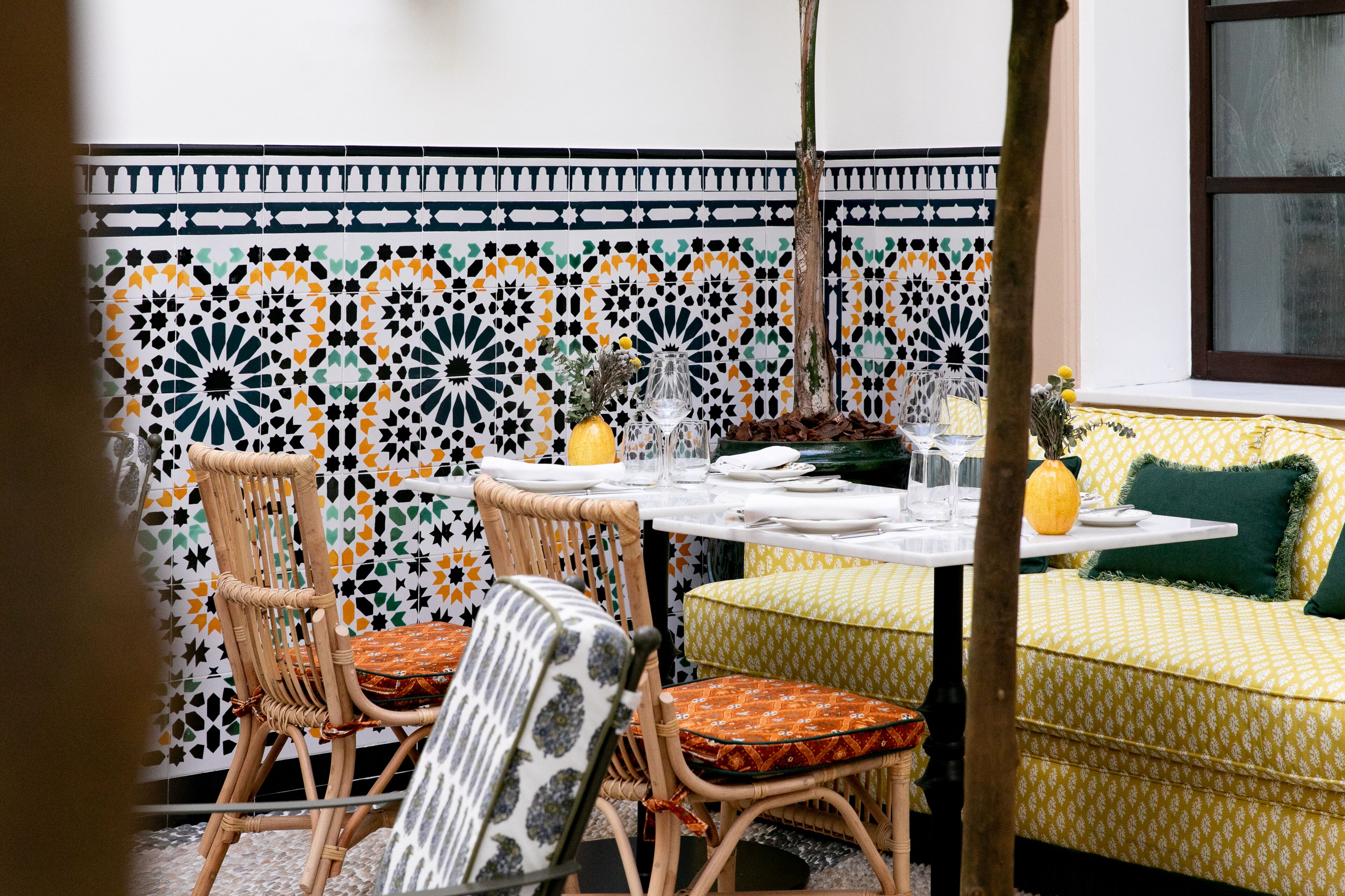 A dining area with a table set for two, surrounded by wicker chairs with patterned cushions.
