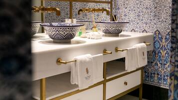 Un baño con dos lavamanos, cada uno con un lavabo de diseño azul y blanco, grifos dorados y una toalla blanca colgada en un toallero dorado.