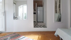 A room with a bed, a mirror, a kitchen area, and a patterned rug. - Παραδοσιακο σπιτι στην καρδια της Υδρας (Hydra island, Saronic Gulf)