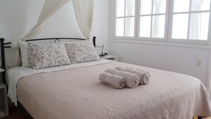 A neatly made bed with a canopy, a bedside table, and a window with curtains. - Παραδοσιακο σπιτι στην καρδια της Υδρας (Hydra island, Saronic Gulf)