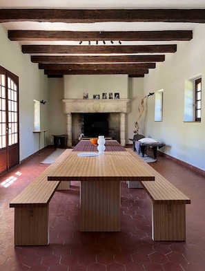 A spacious room with a large wooden table, benches, a fireplace, and a tiled floor.