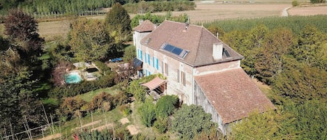 Une grande maison avec un toit en pente, entourée d’un jardin et d’une piscine.