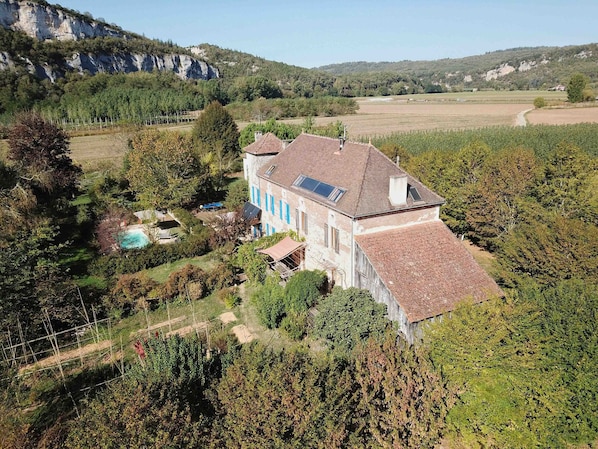 A large house with a sloped roof, surrounded by a garden and a swimming pool.