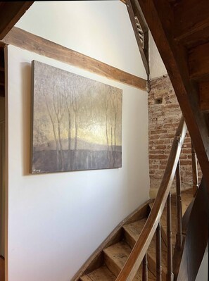 A staircase with wooden steps and a handrail, leading to a room with a white wall and a large abstract painting.