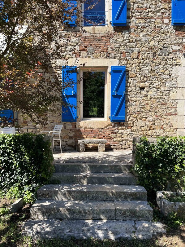 A stone building with blue shutters, a small bench, and steps leading to a door.