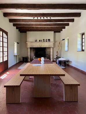 A spacious room with a large wooden table, benches, a fireplace, and a tiled floor.