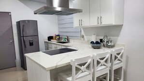 Une cuisine moderne avec des meubles blancs, une hotte en acier inoxydable, un réfrigérateur encastré, un plan de travail en marbre et un tabouret de bar blanc.