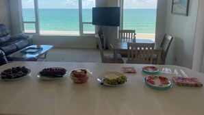 Un salon doté d’une grande fenêtre donnant sur l’océan, une table à manger avec différents plats, et un canapé en cuir.