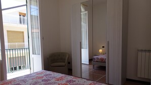 Een slaapkamer met een bed, een stoel, een grote spiegel en uitzicht op een balkon.