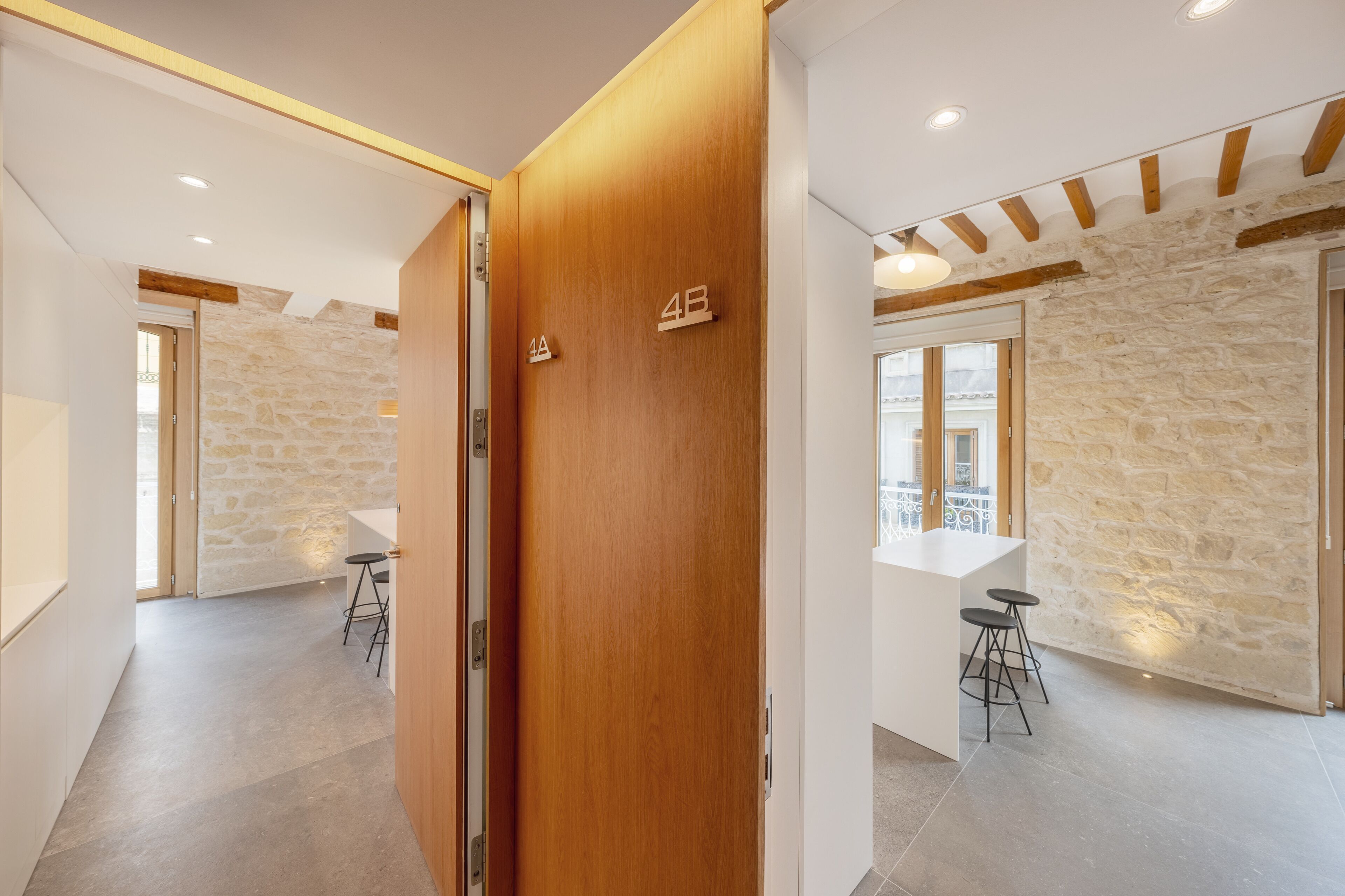 A modern hotel room with a stone wall, wooden door, and a bar area with stools.