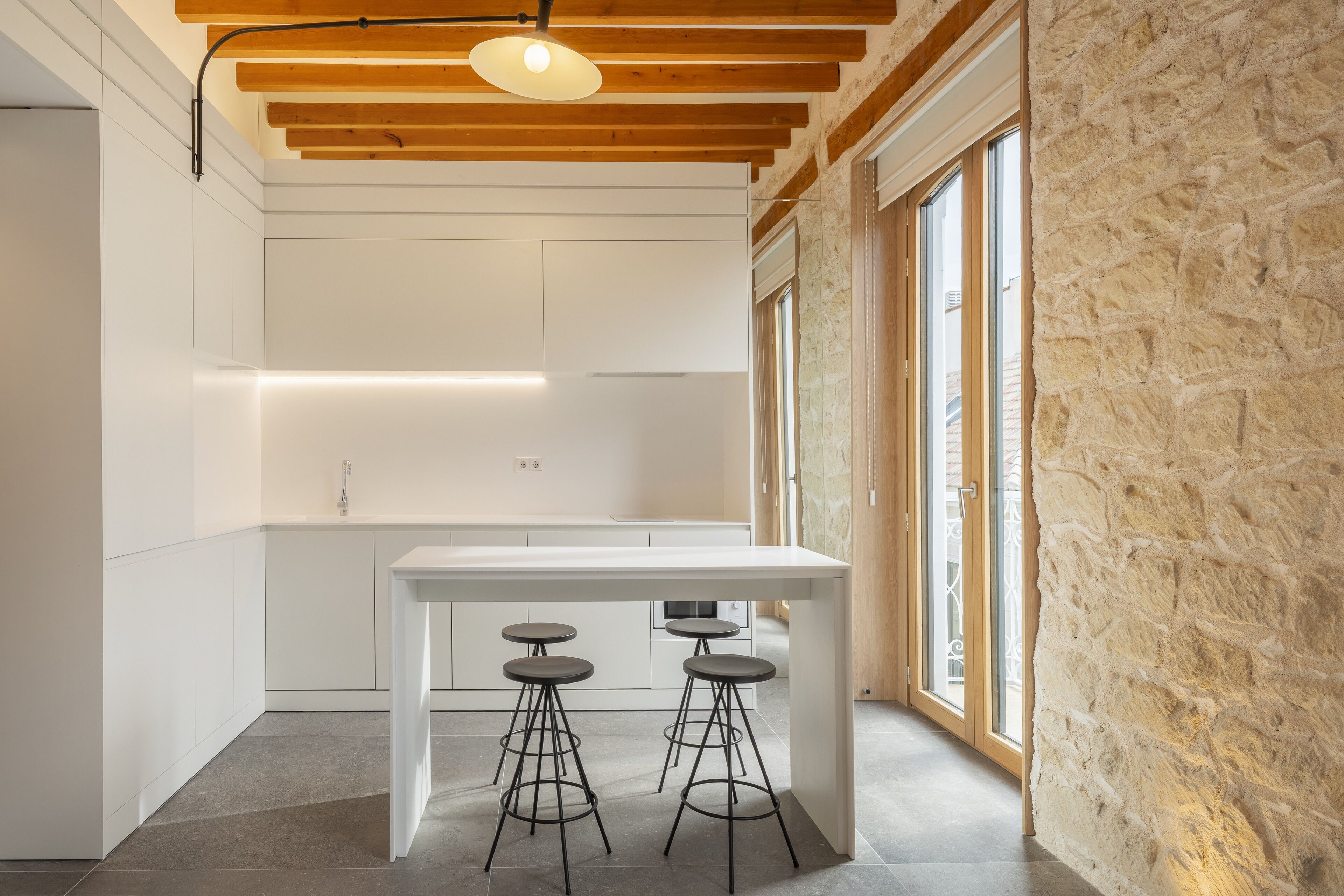 Una cocina moderna con una isla central, taburetes de bar y ventanas amplias.